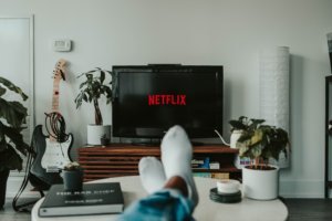 A photo of a living room with a pictured television, plants and guitar.