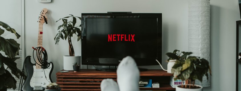 A photo of a living room with a pictured television, plants and guitar.