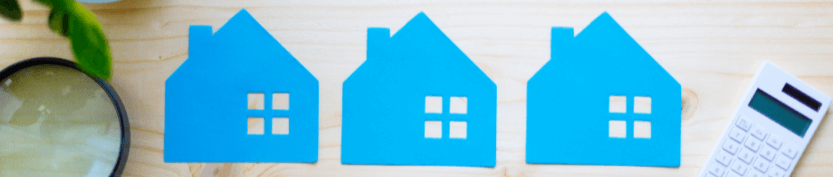 A magnifying glass with three identical blue house cutouts along with a calculator resting on a wood table