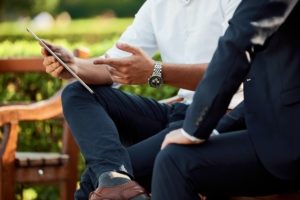 Two individuals sitting on a bench reviewing information on a tablet