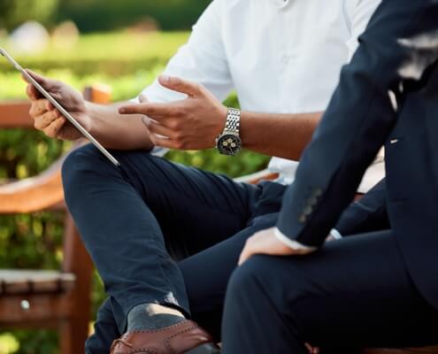 Two individuals sitting on a bench reviewing information on a mobile device