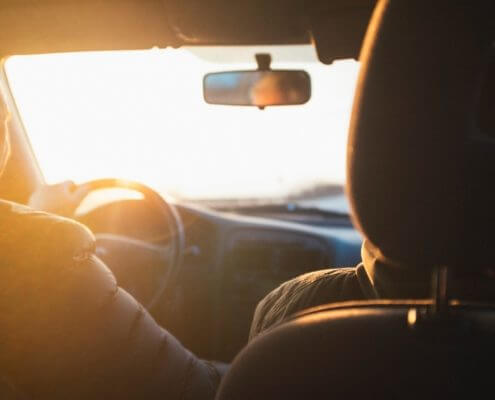 A photo taken from the backseat of a car picturing a person driving a car